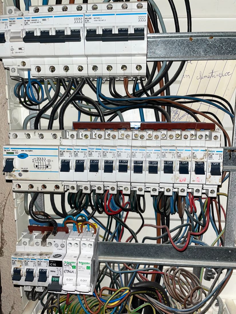 Tableau Hager chargé de câbles, avec un circuit de climatiseur noté à la main.
