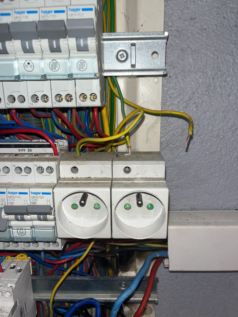 Deux prises modulaires dans un tableau Hager, avec des fils de terre dénudés non raccordés.